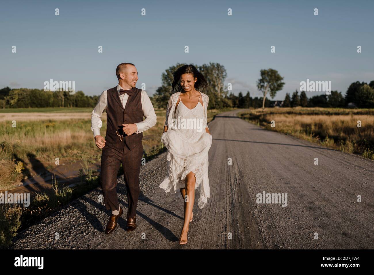 Felice sposa e sposo che corrono su strada durante la giornata di sole Foto Stock