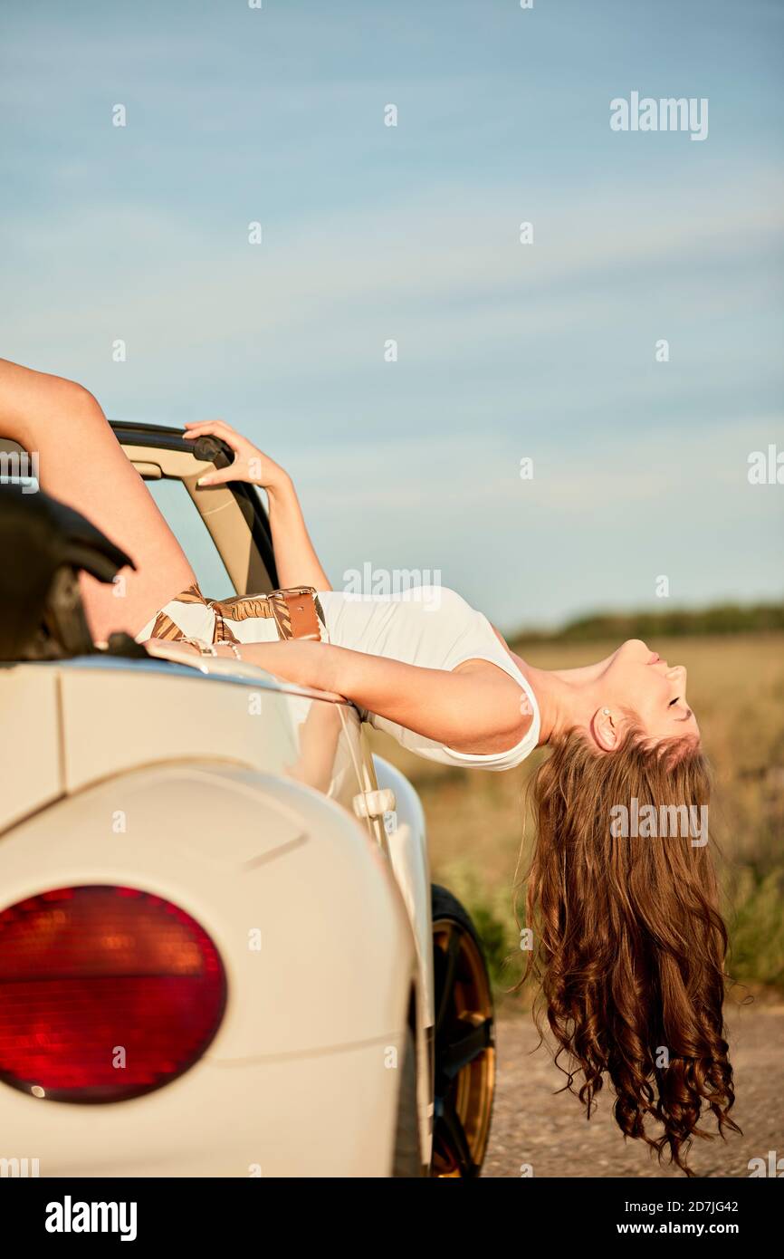 Bella donna con lunghi capelli ricci che si inclinano fuori di convertibile auto Foto Stock