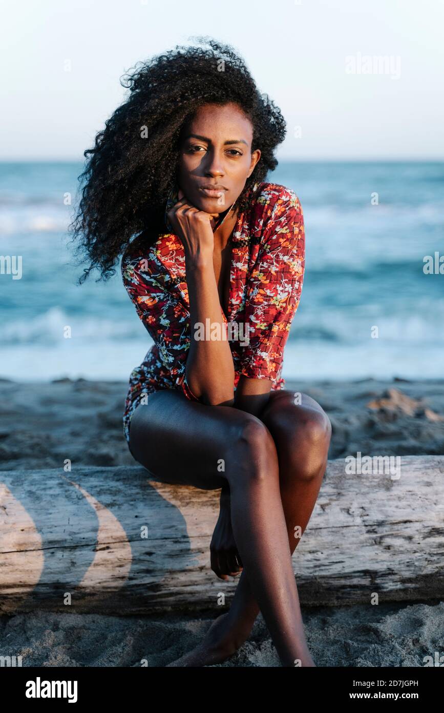 Giovane donna con la mano sul mento seduto in spiaggia durante giorno di sole Foto Stock