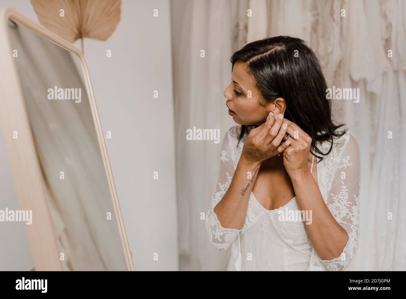 Giovane sposa che indossa orecchini mentre si guarda nello specchio al matrimonio negozio di abbigliamento Foto Stock