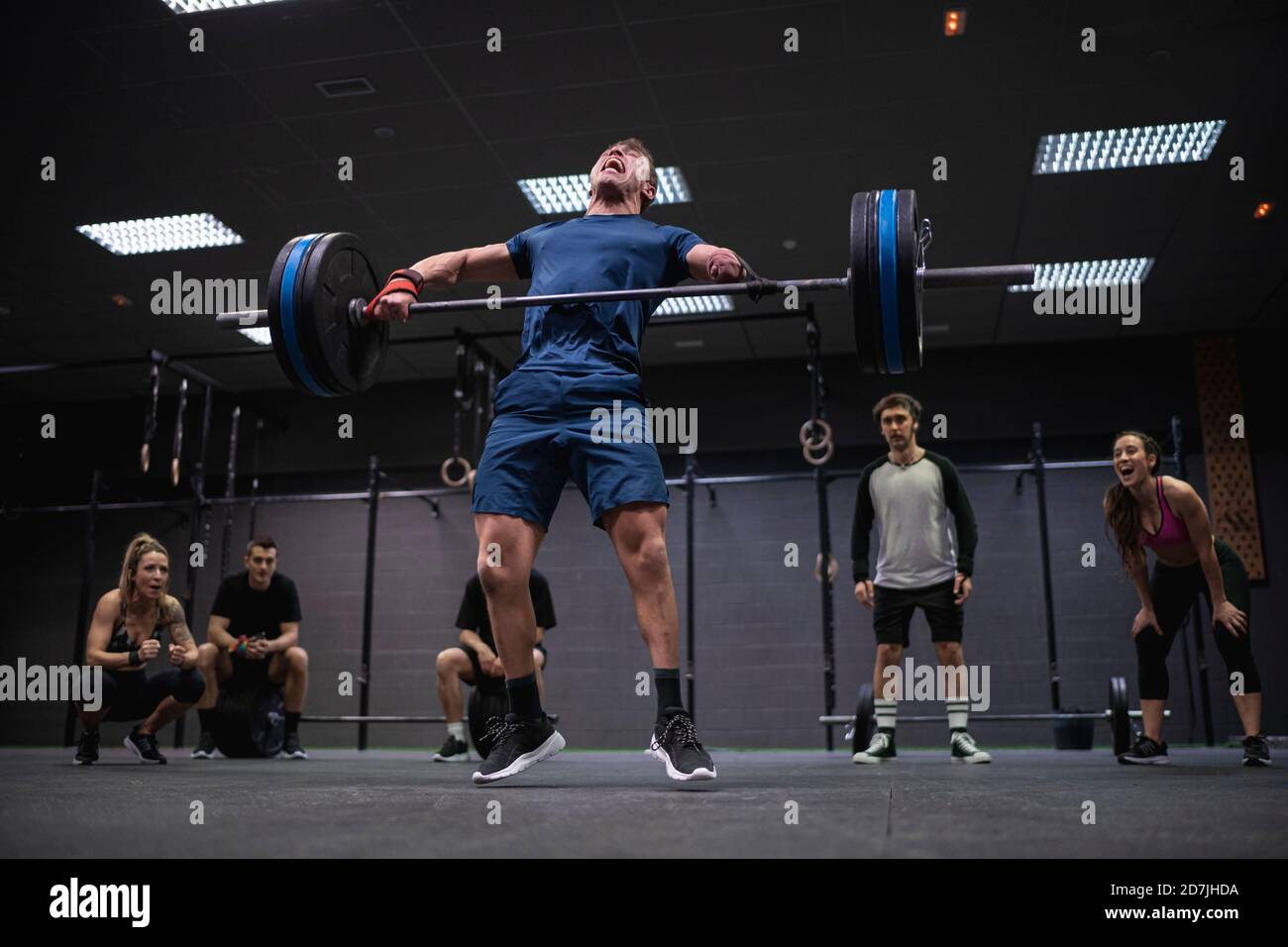 Atleta adattiva che salta mentre solleva il barbell con le persone che si acclamano sfondo in palestra Foto Stock