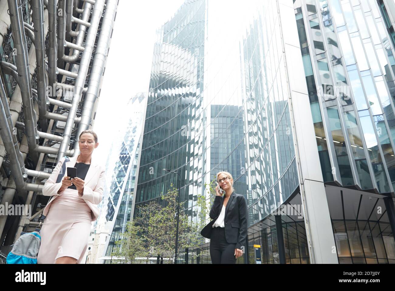 Donne d'affari che usano i telefoni cellulari contro gli edifici degli uffici in città Foto Stock