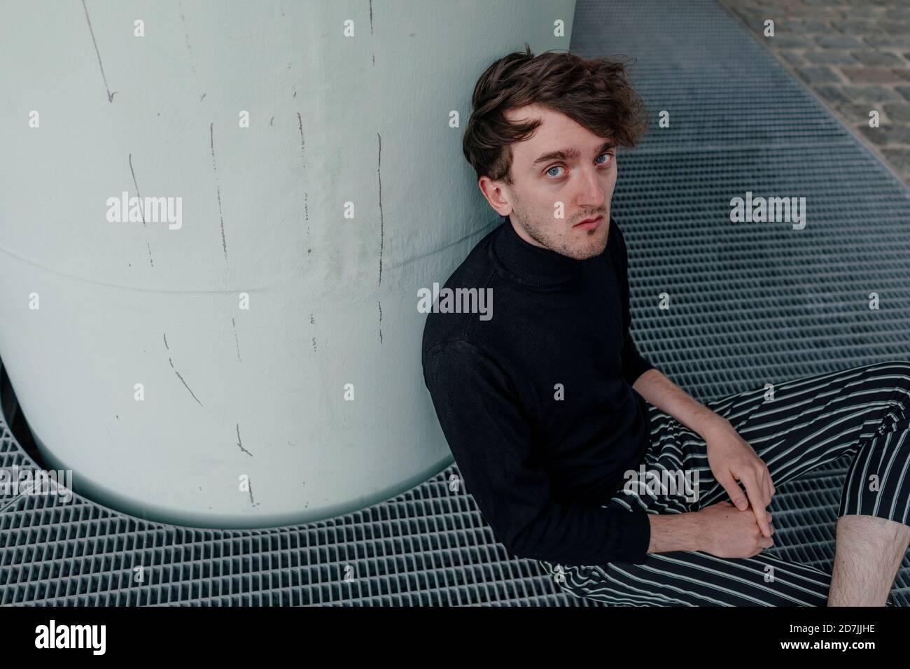 Giovane uomo con occhi blu seduto per colonna sul sentiero Foto Stock