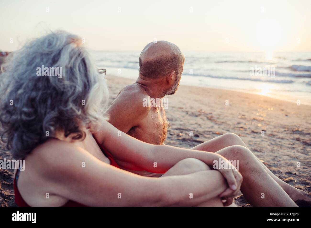 Coppia senior che ammirano la vista del tramonto mentre si siede in spiaggia Foto Stock