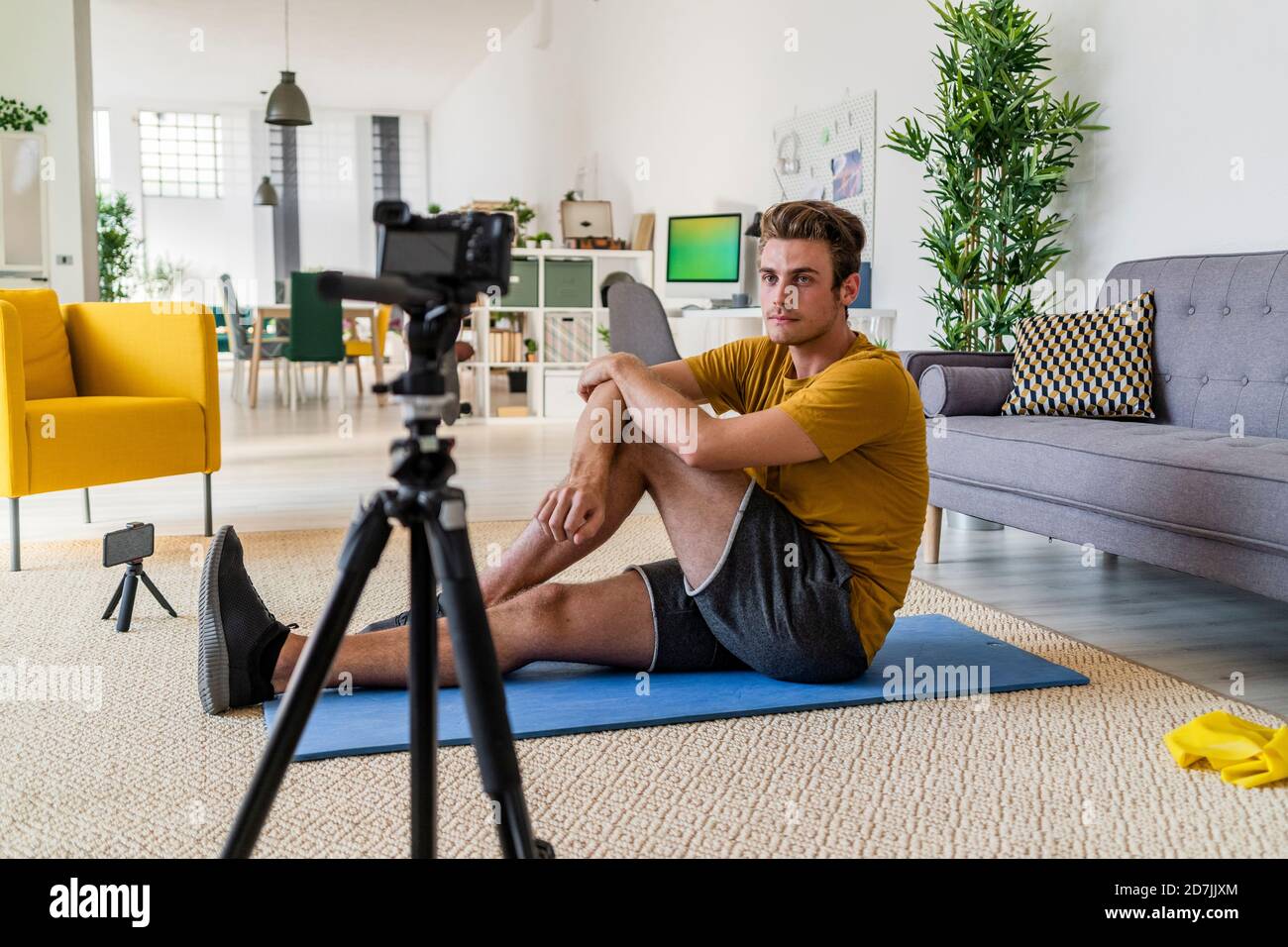 Fitness Trainer che registra l'esercizio sulla fotocamera mentre si è seduti sul tappetino a casa Foto Stock