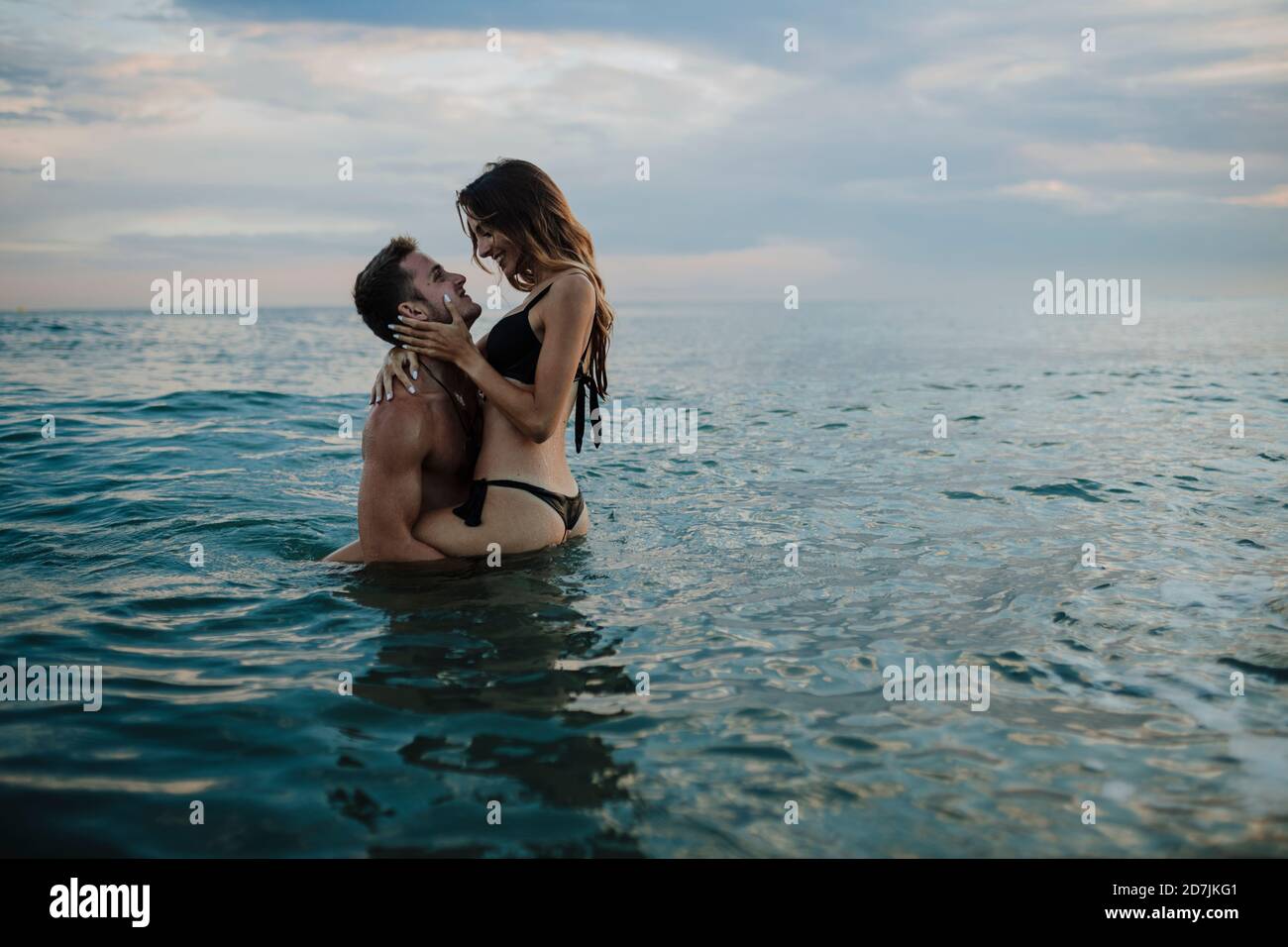 Giovane coppia che fa romanticismo in acqua alla spiaggia durante il tramonto Foto Stock