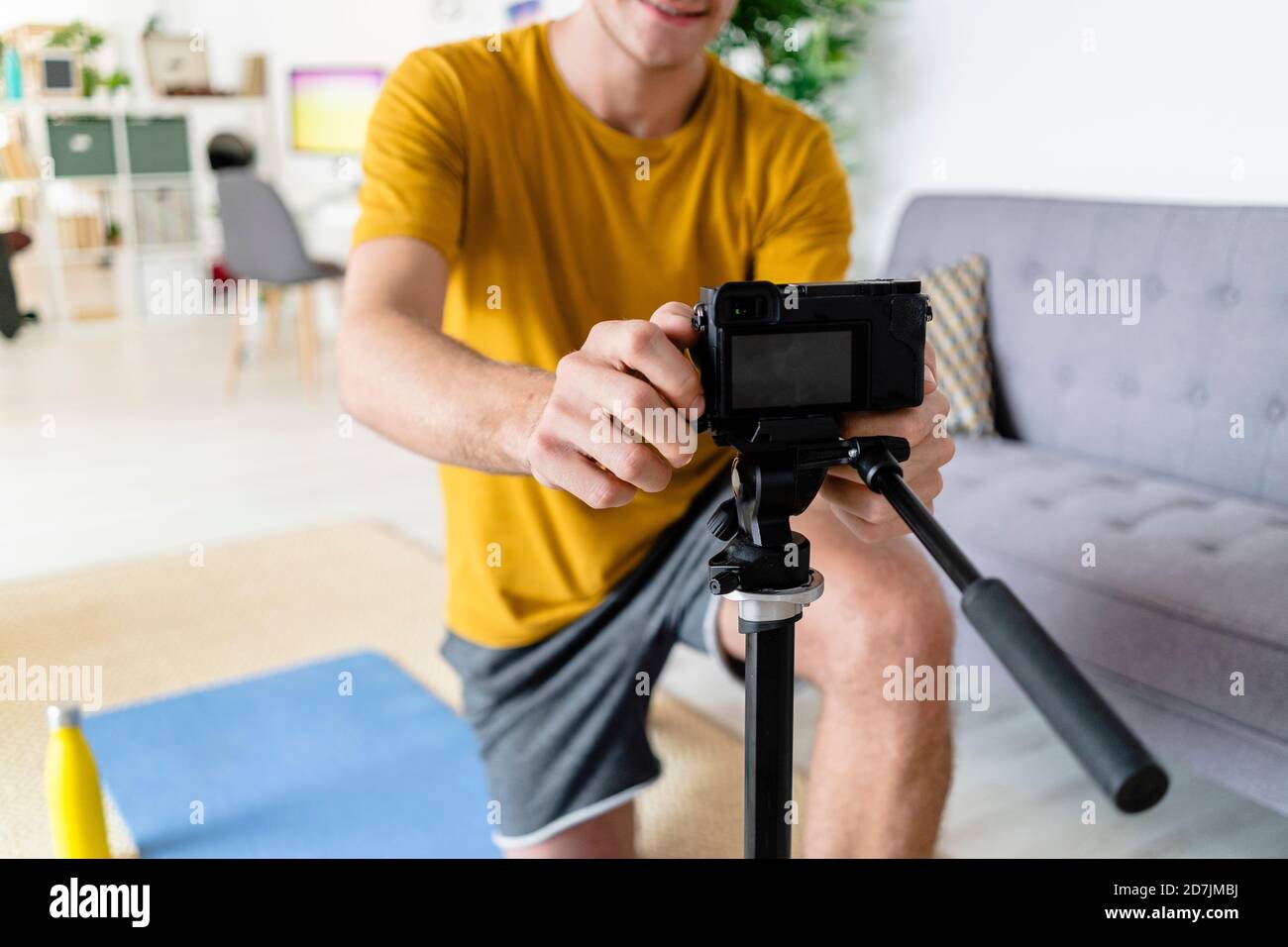 Giovane uomo che regola la videocamera mentre è seduto a casa Foto Stock