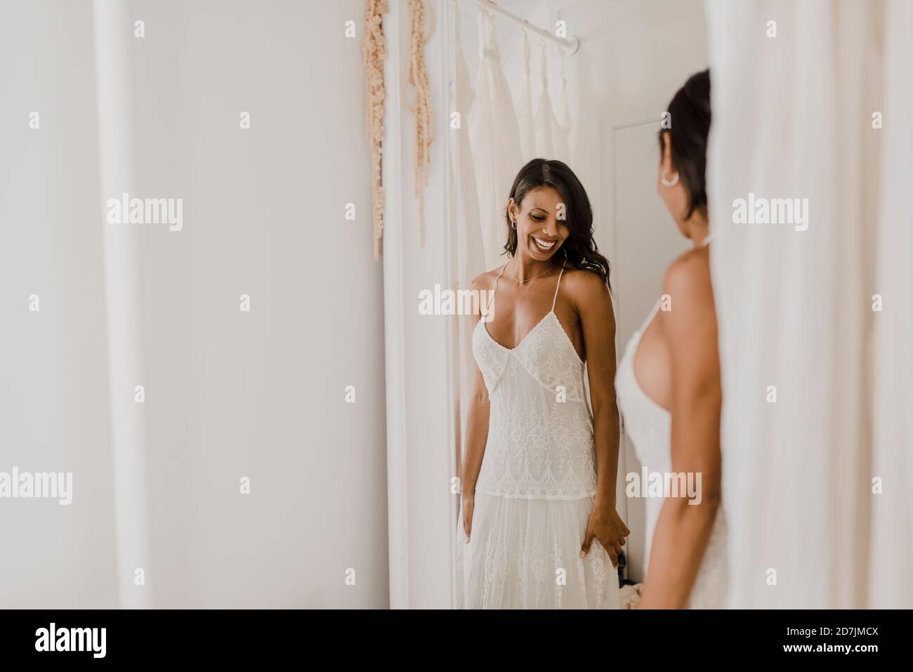 Sposa sorridente che guarda nello specchio mentre si sta in piedi al vestito da sposa negozio Foto Stock