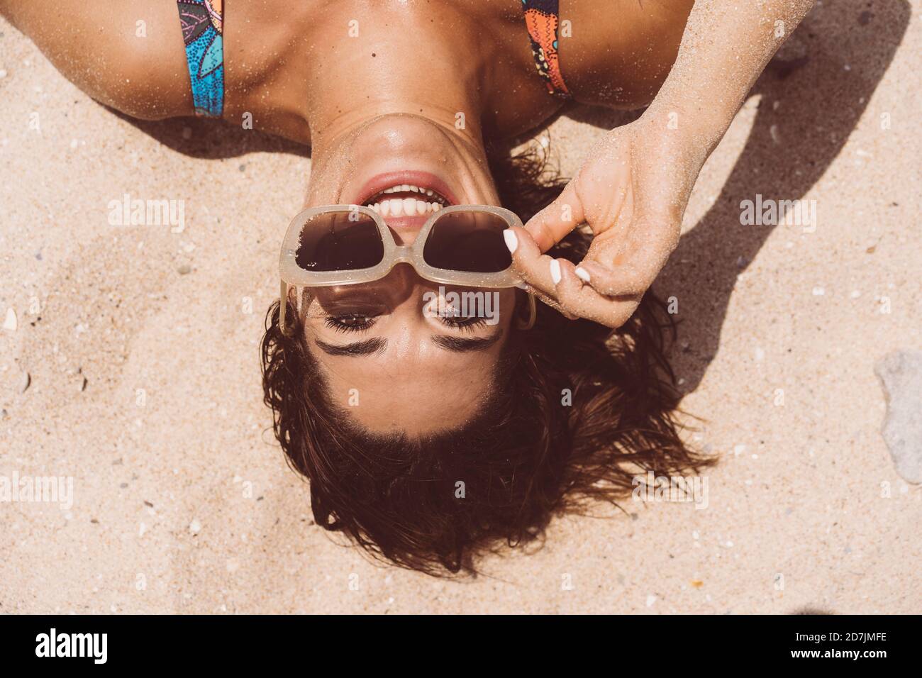 Donna allegra che indossa occhiali da sole mentre si sdraia sulla spiaggia di Valdevaqueros in giornata di sole, Tarifa, Spagna Foto Stock