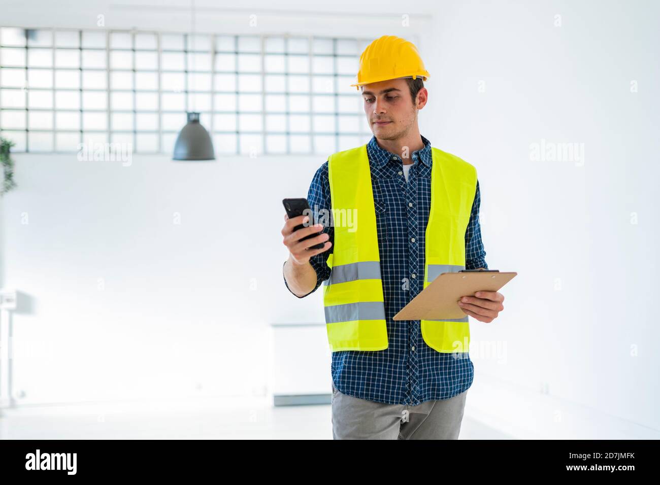 Giovane uomo che indossa casco e giacca da lavoro con cellulare telefono mentre si è in piedi in cantiere Foto Stock