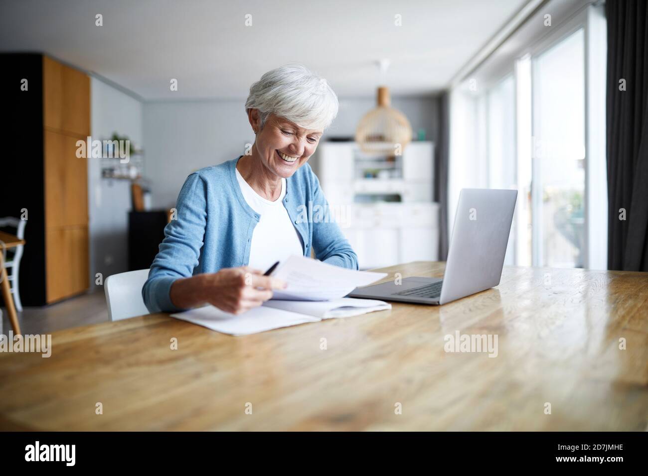 Sorridente donna anziana attiva che fa lavoro di carta mentre si siede a. casa Foto Stock