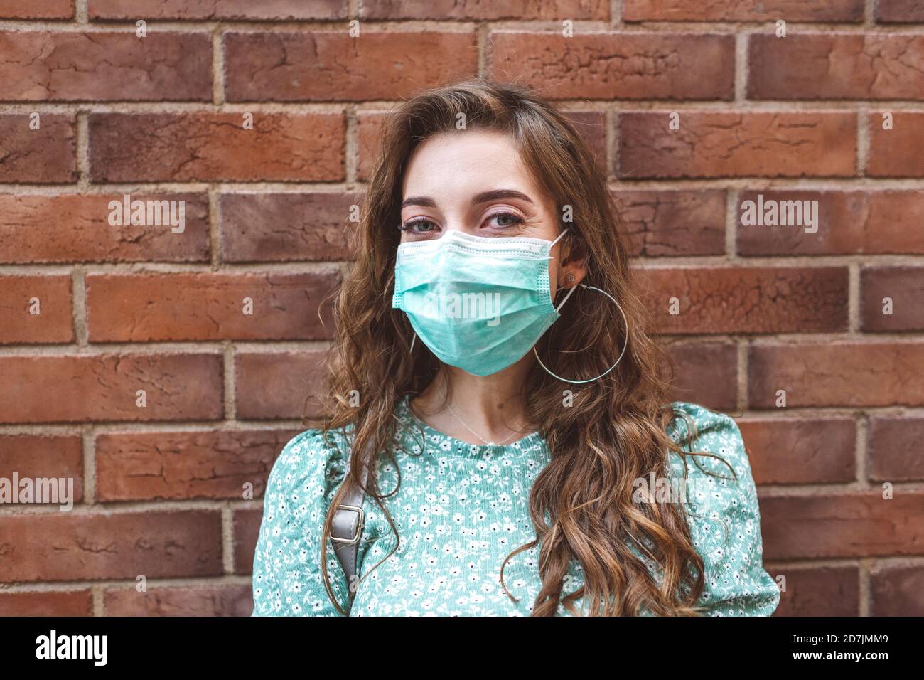 Donna che indossa la maschera contro la parete di mattoni durante l'epidemia di COVID-19 Foto Stock