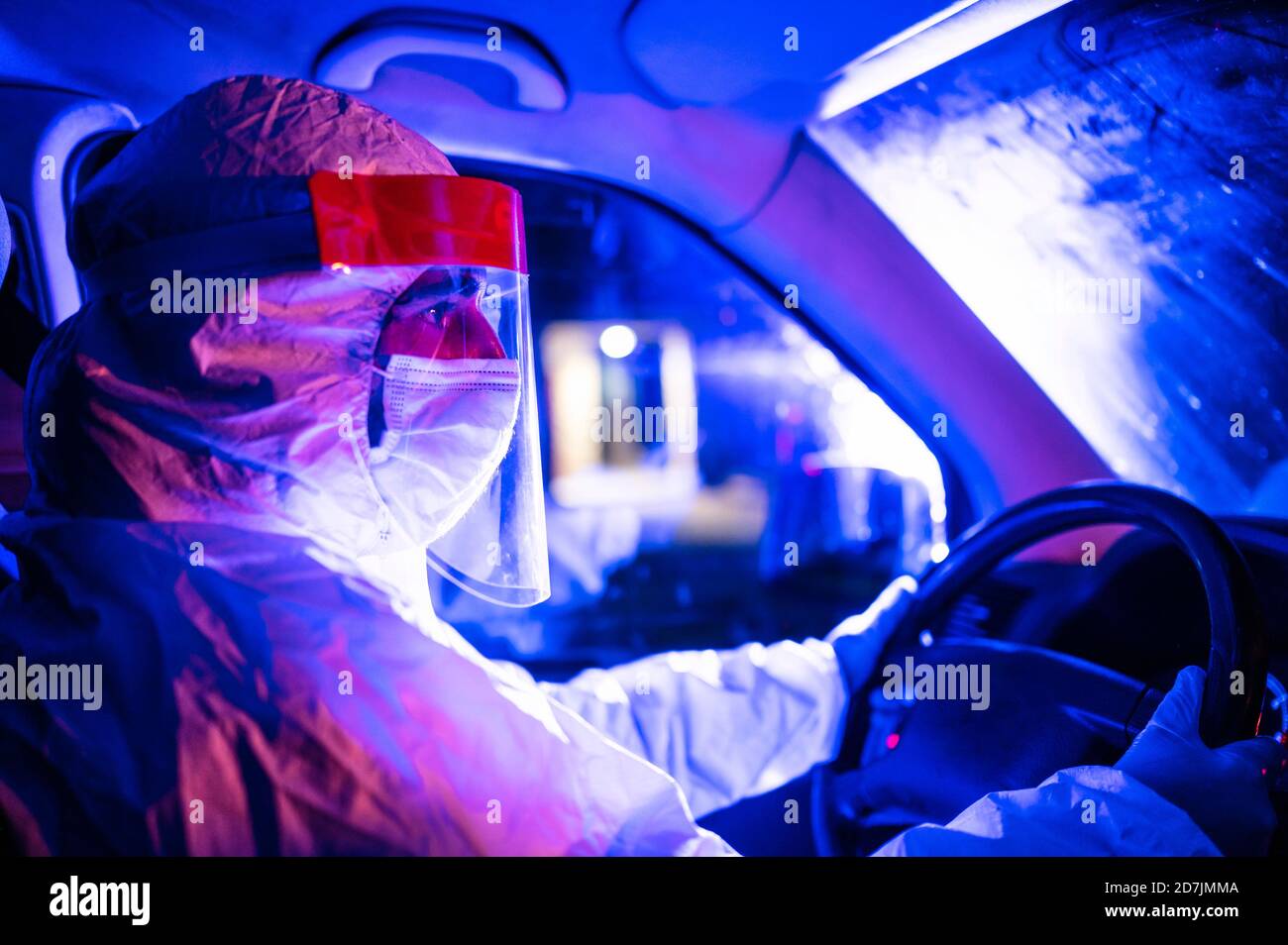 Uomo medio adulto che indossa un vestito protettivo che guida l'ambulanza di notte Foto Stock