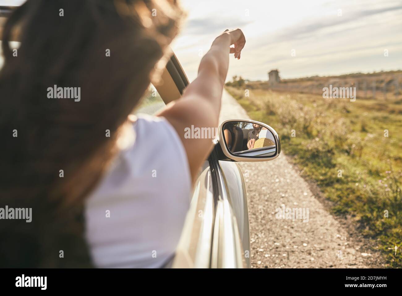 Giovane donna che punta verso il cielo nuvoloso mentre si siede in auto Foto Stock