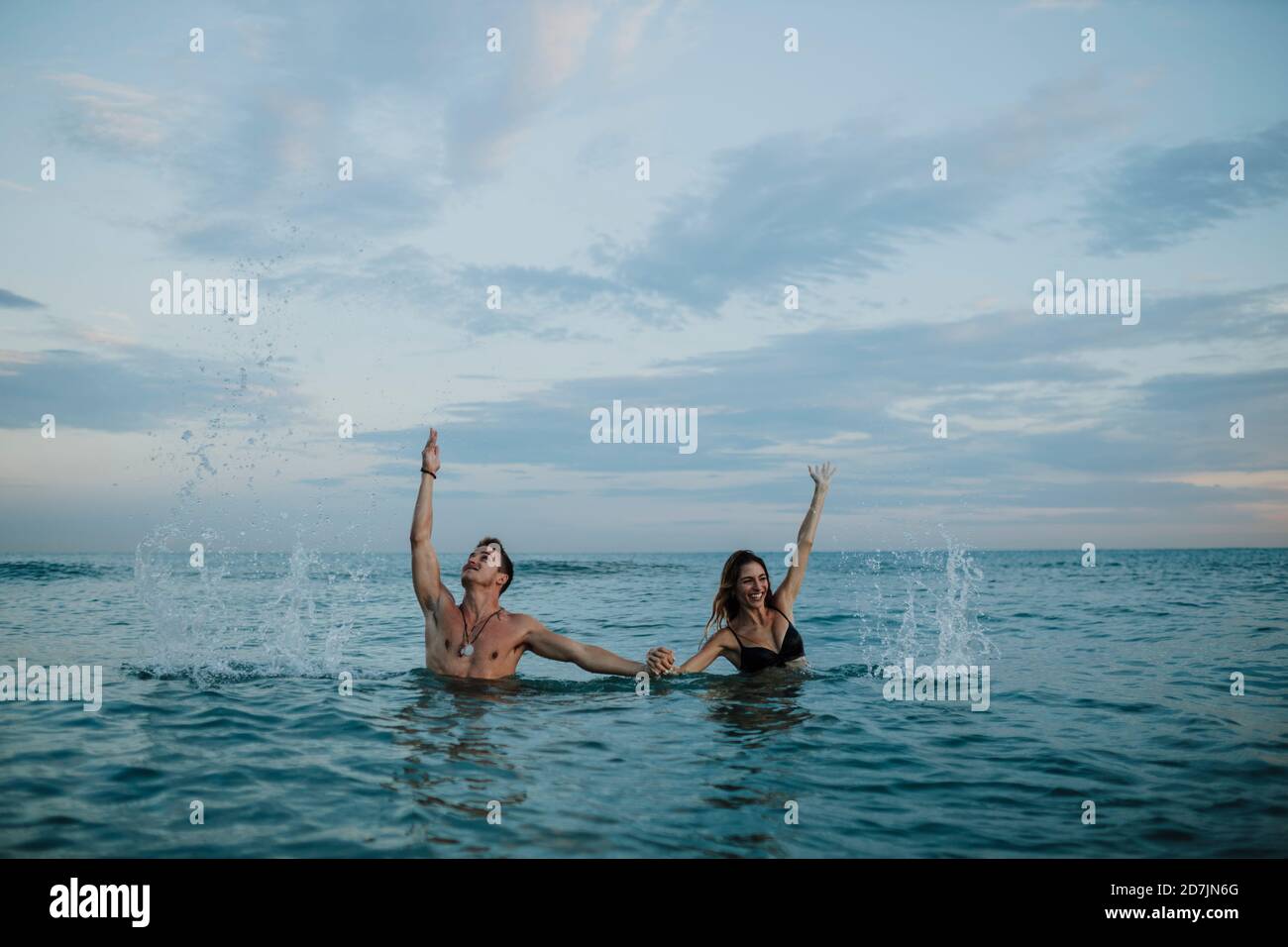 Una coppia giocosa che tiene la mano mentre si sta in acqua Foto Stock