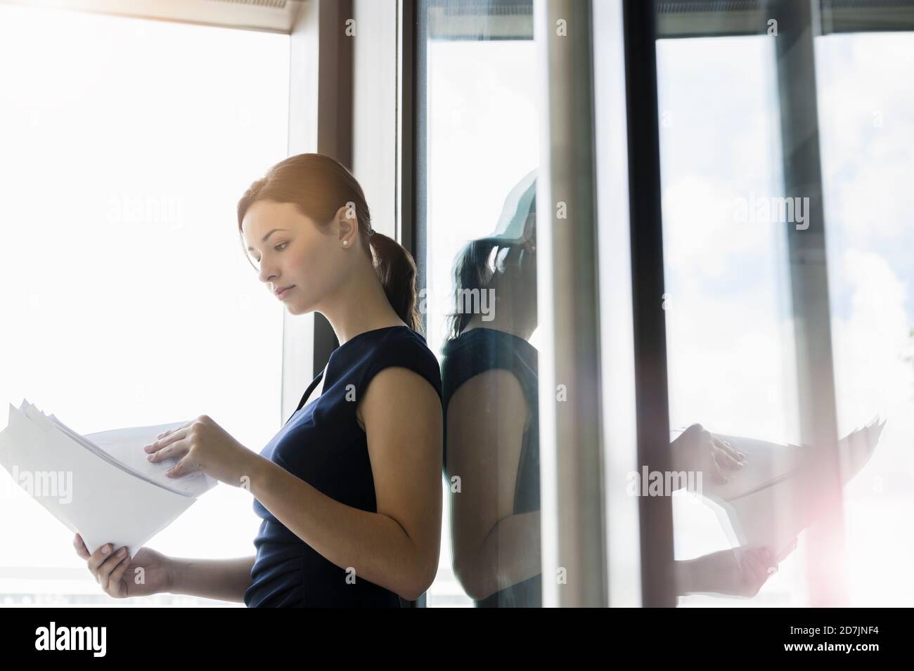 Donna d'affari che analizza i rapporti mentre si è in piedi dalla finestra in ufficio Foto Stock