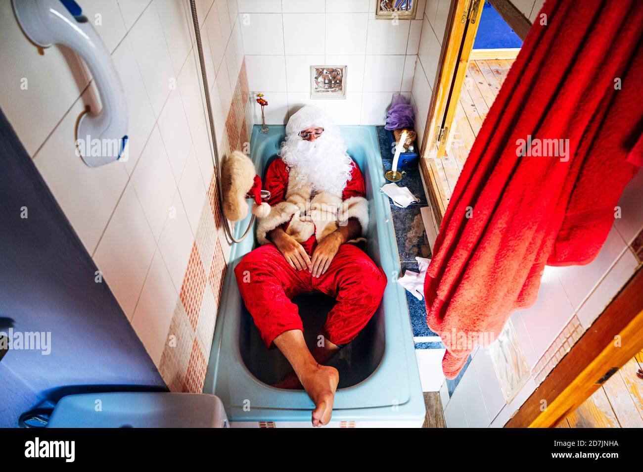 Uomo che indossa il costume di Babbo Natale sdraiato nella vasca da bagno a casa Foto Stock