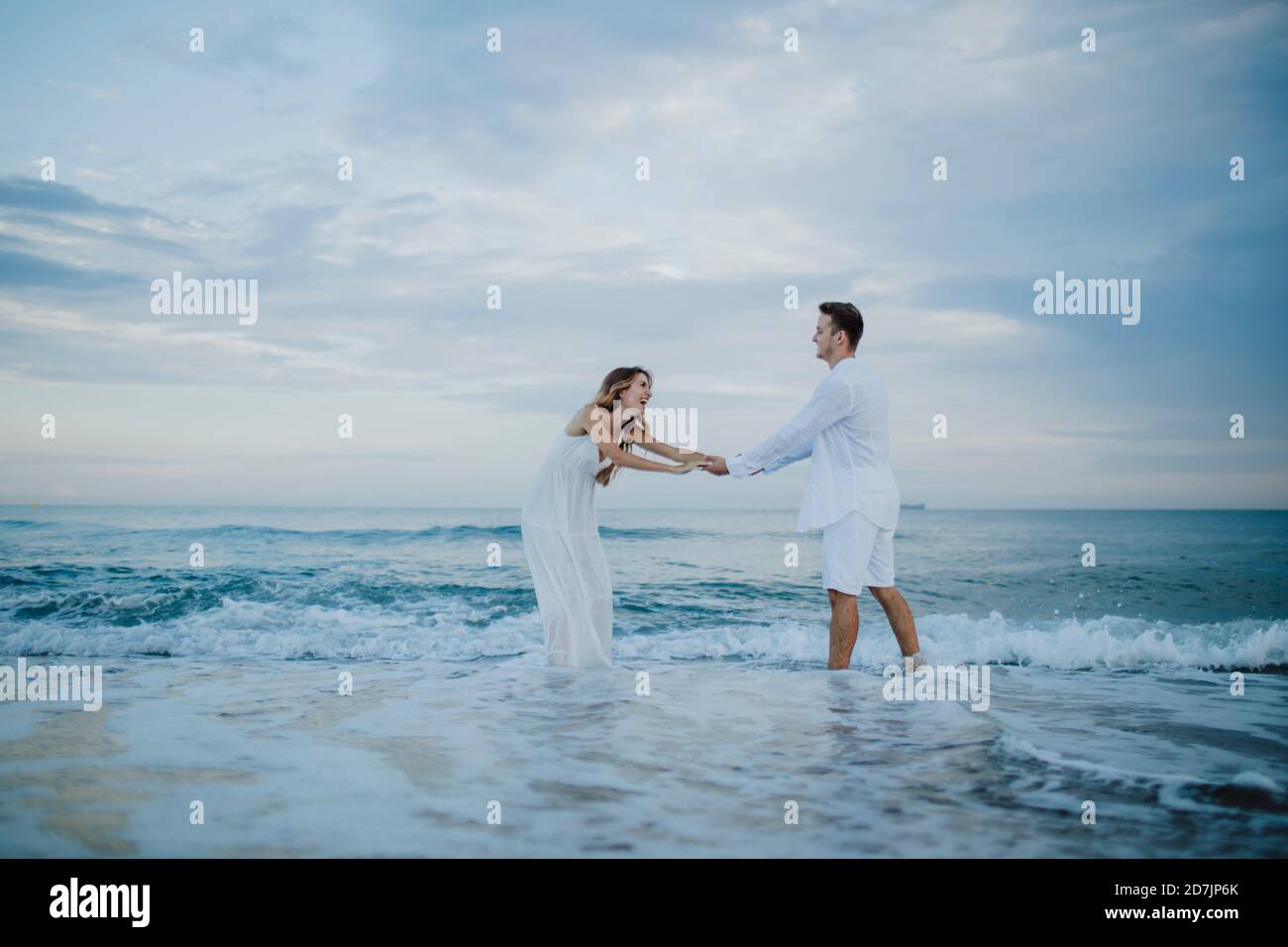 Una coppia giocosa che tiene le mani mentre si è in piedi in acqua sulla spiaggia Foto Stock