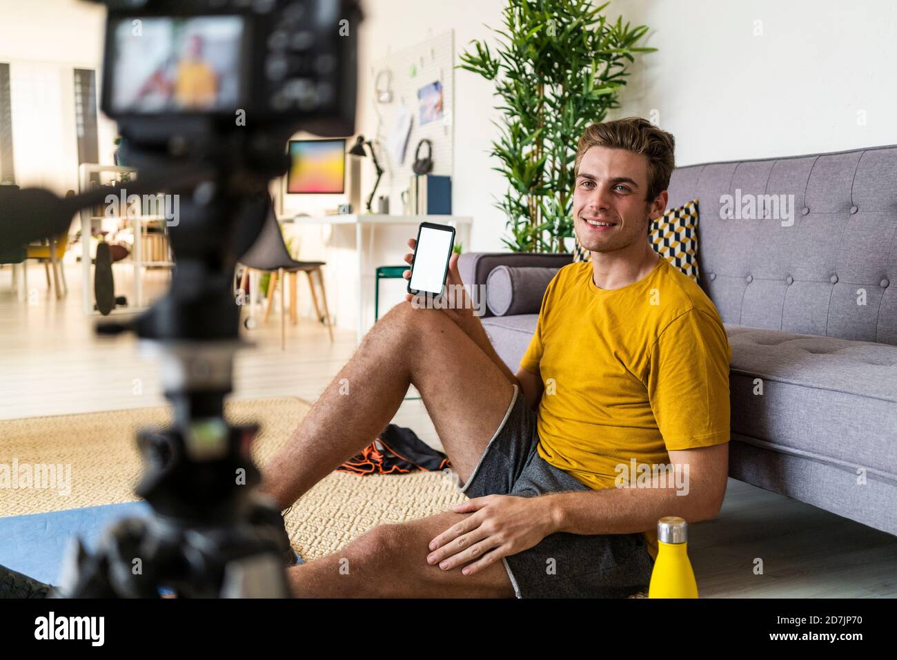 Un istruttore sorridente che mostra il telefono cellulare alla fotocamera mentre si è seduti a. casa Foto Stock