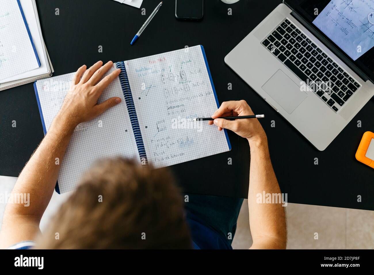 Studente di sesso maschile che risolve equazioni matematiche nel libro degli esercizi mentre si siede a. tabella Foto Stock