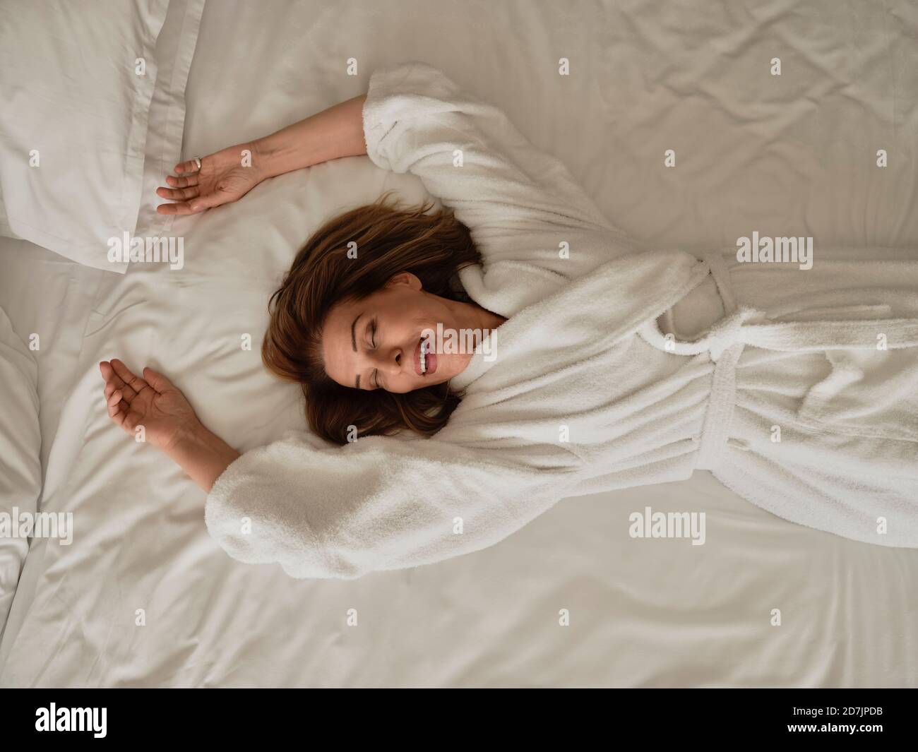 Donna anziana sorridente sdraiata su un letto bianco in un hotel di lusso camera Foto Stock