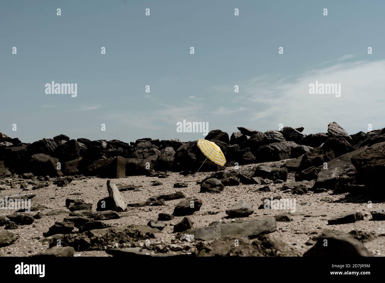 Ombrello giallo sulla sabbia tra le rocce sulla spiaggia contro il cielo durante il giorno di sole Foto Stock