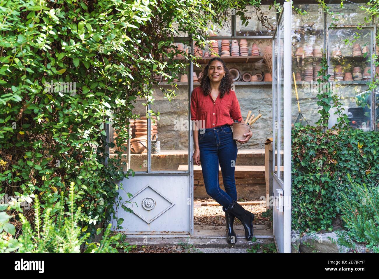 Donna matura in piedi con attrezzatura da giardinaggio sulla porta del giardino capanna Foto Stock