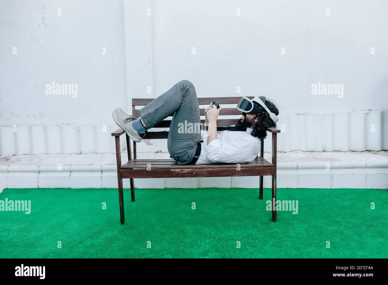 Uomo che indossa occhiali di realtà virtuale giocando a gioco mentre si sdraiava panca cortile Foto Stock