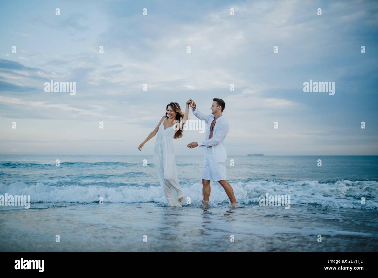 Giovane coppia che gira donna mentre balla in acqua in spiaggia Foto Stock