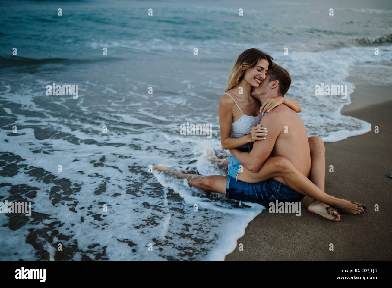 La coppia si abbraccia mentre si siede al bordo dell'acqua sopra spiaggia Foto Stock