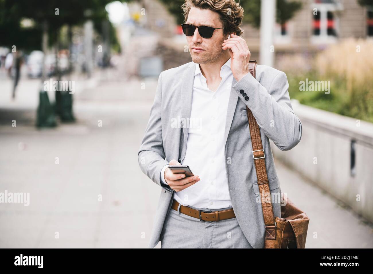 Uomo d'affari che collega le cuffie intrauricolari con il telefono cellulare mentre si sta in piedi marciapiede in città Foto Stock