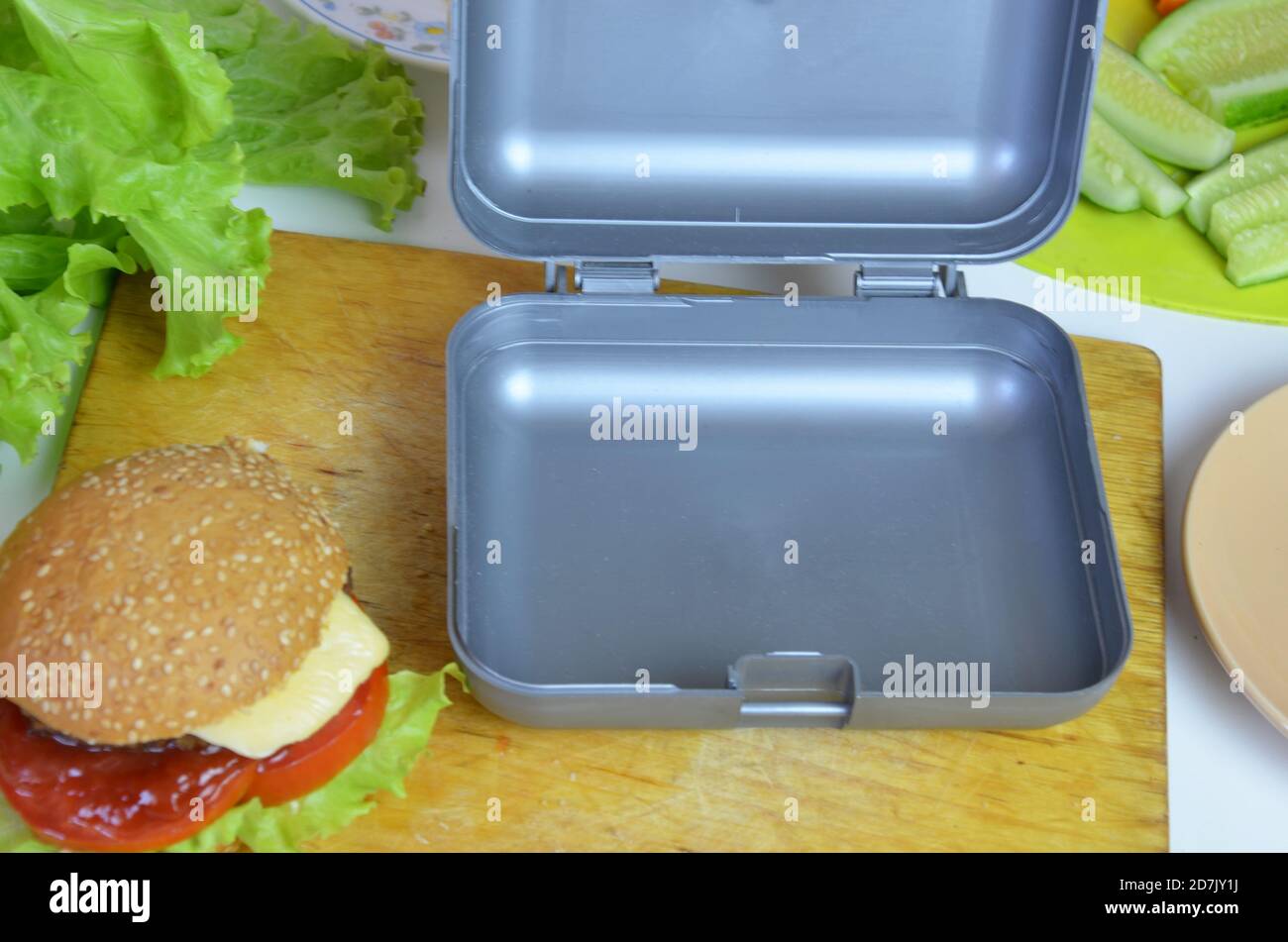 Hamburger fatti in casa con lattuga in scatola sul tavolo. Con succo d'arancia giallo brillante. Con noci alla banana. Carote e cetrioli di verdure a fette Foto Stock
