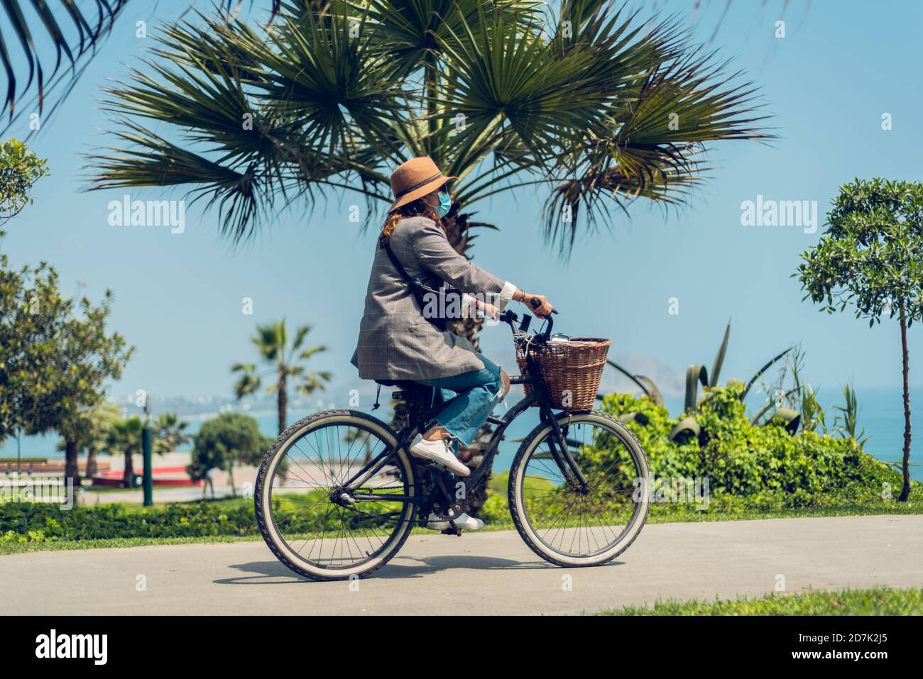 Donna guida una bicicletta e si protegge con una maschera viso nel parco. Nuovo concetto di normalità Foto Stock