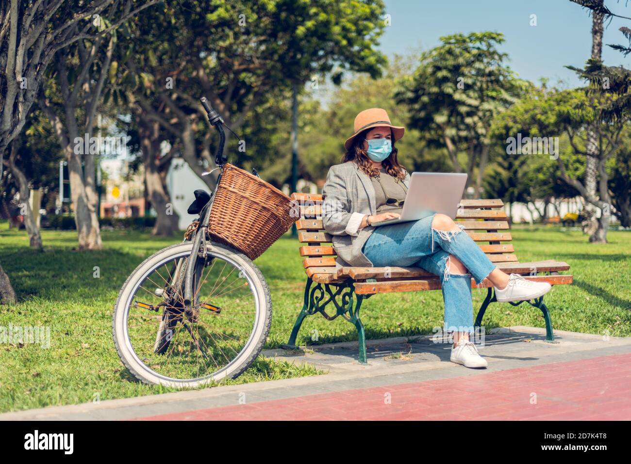 Donna lavora seduto in un parco e si protegge con una maschera medica. Ritratto di una donna alla moda che ama gli spazi aperti e scrive sul suo blog Foto Stock