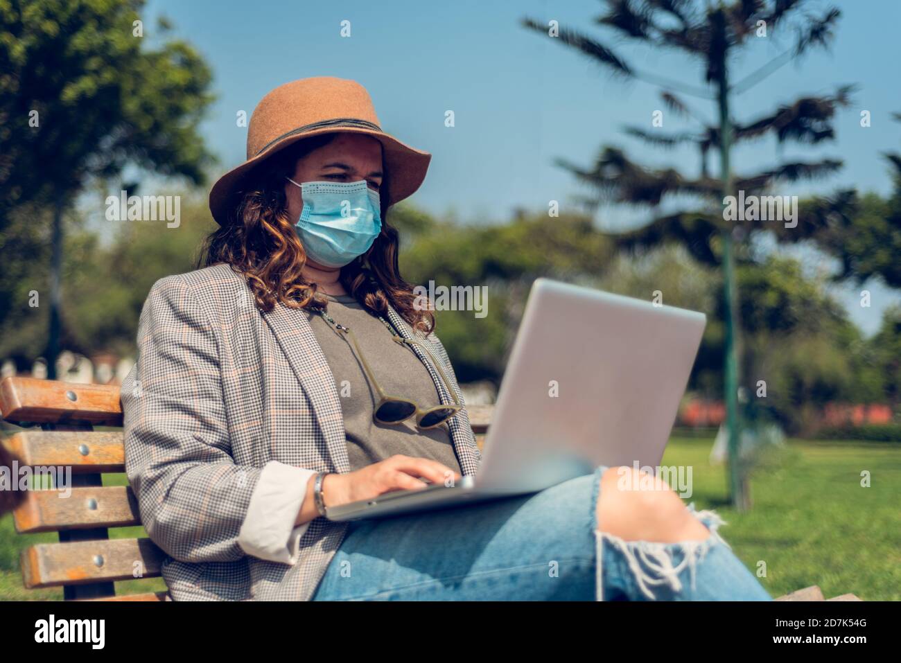 Donna lavora seduto in un parco e si protegge con una maschera medica. Ritratto di una donna alla moda che ama gli spazi aperti e scrive sul suo blog Foto Stock