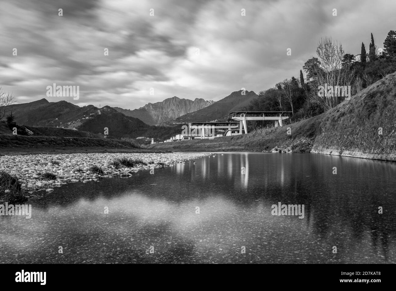 Un fiume in Versilia con aziende di lavorazione del marmo e il Alpi Apuane sullo sfondo - bianco e nero Foto Stock