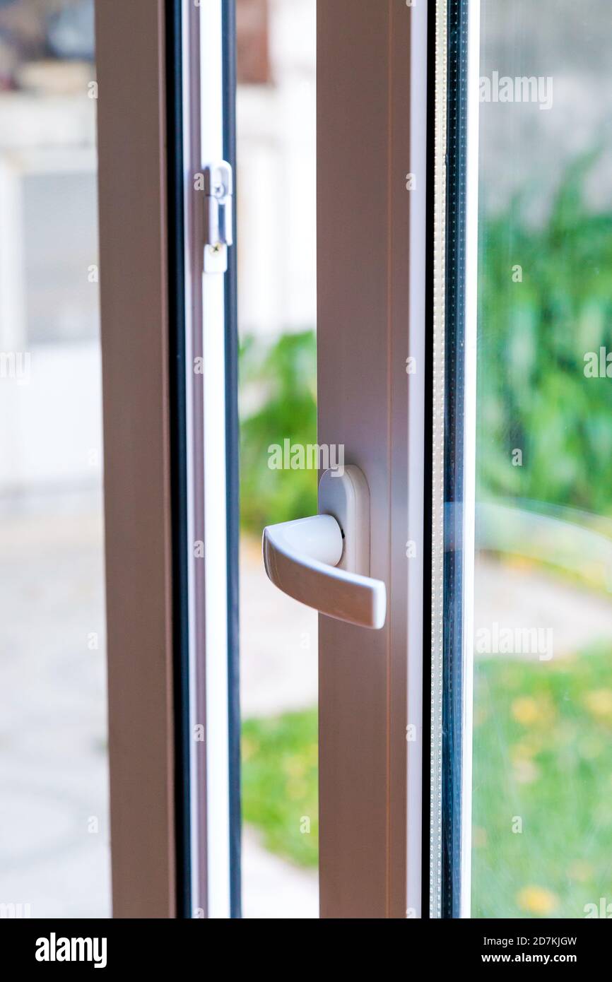 Aprire la porta di una casa di famiglia. Close-up della serratura sulla porta scorrevole con il cantiere di sfondo. PVC bianco e porta a doppio vetro. Foto Stock
