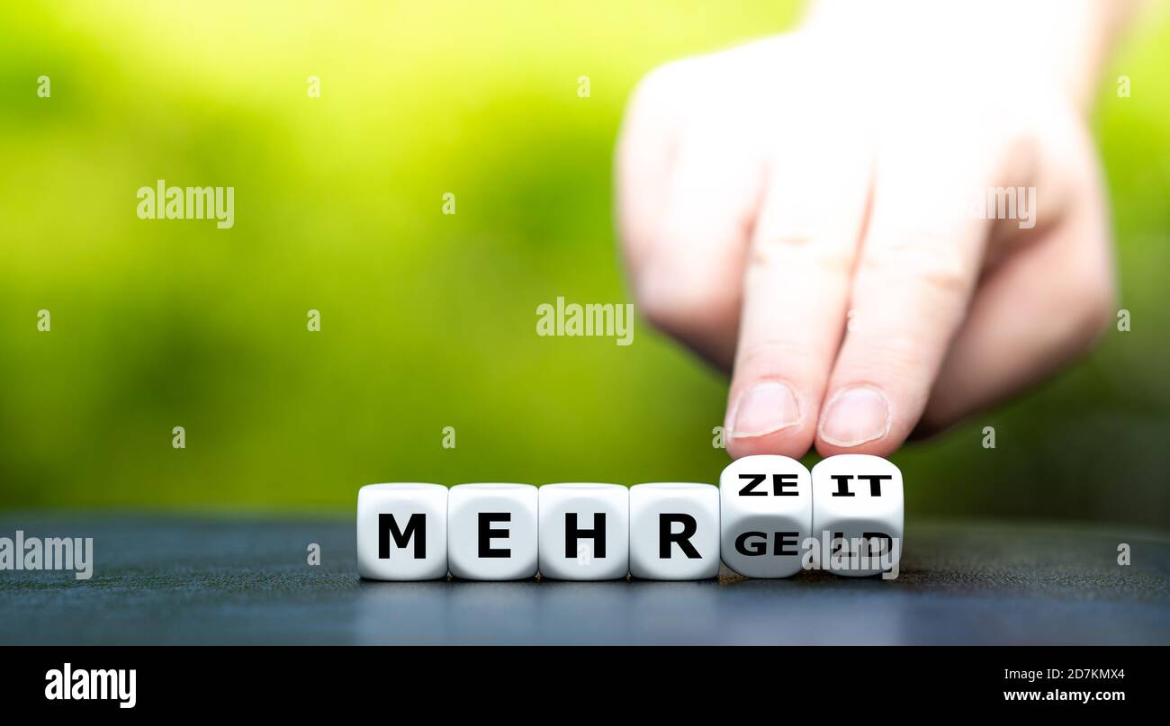 La mano trasforma i dadi e cambia l'espressione tedesca 'ehr Geld' (più soldi) in 'ehr Zeit' (più tempo). Foto Stock