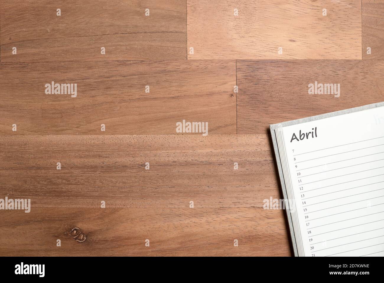 Pagina vuota di un pianificatore giornaliero in spagnolo per il mese di aprile, su una scrivania di legno. Disposizione piatta con spazio per la copia Foto Stock