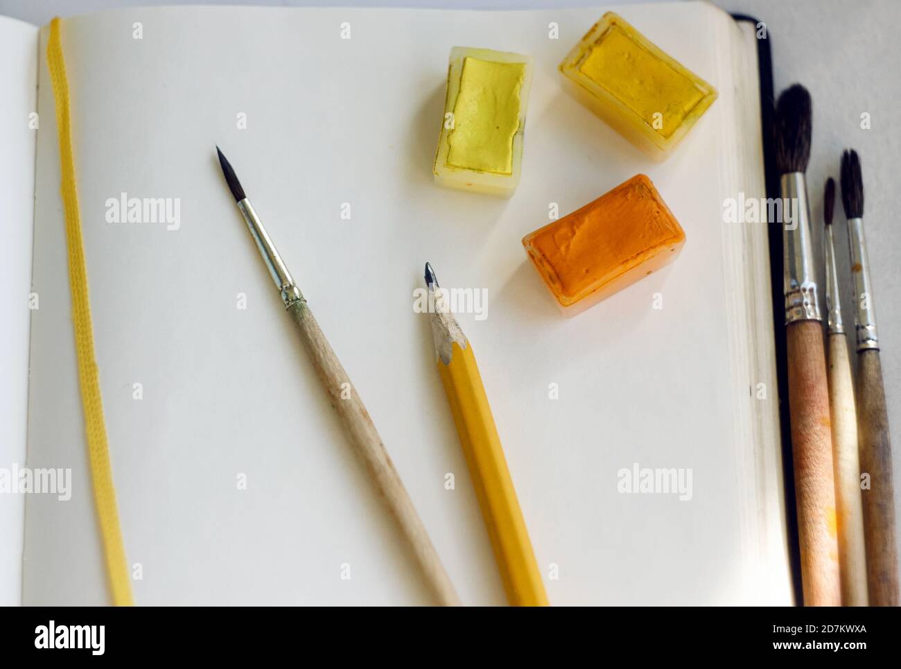 Su un taccuino aperto con un segnalibro giallo sono vernici acquerello in cuvette, pennelli da capelli scoiattolo e una semplice matita per disegnare. Tutto io Foto Stock