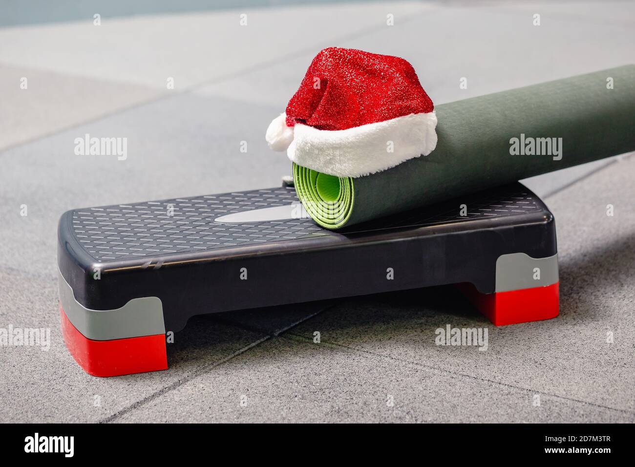 Primo piano di tappetino grigio con cappello Babbo Natale in palestra. Miglior regalo di Natale per una persona attiva. Concetto di yoga xmas. Foto Stock