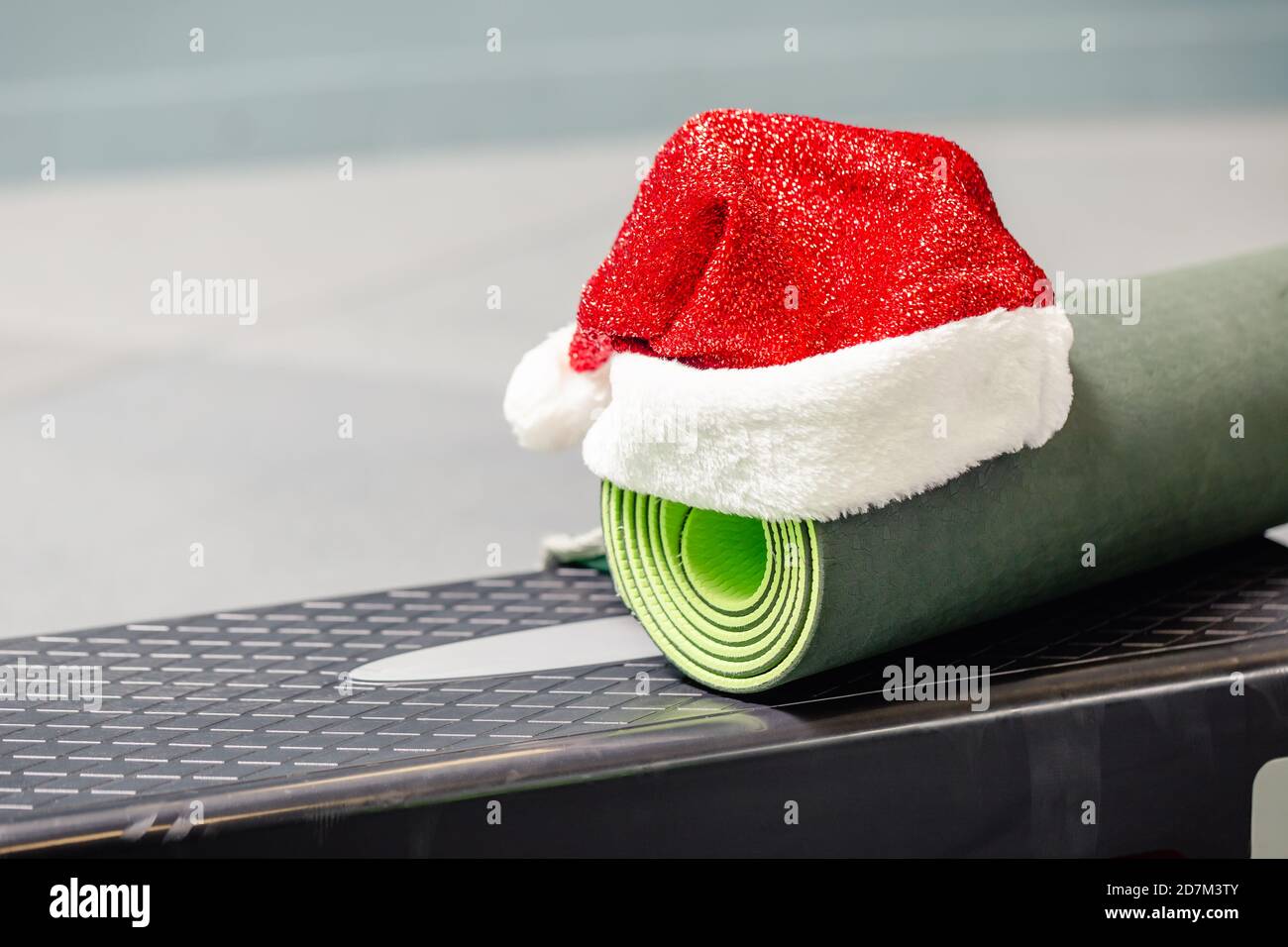 Primo piano di tappetino grigio con cappello Babbo Natale in palestra. Miglior regalo di Natale per una persona attiva. Concetto di yoga xmas. Foto Stock