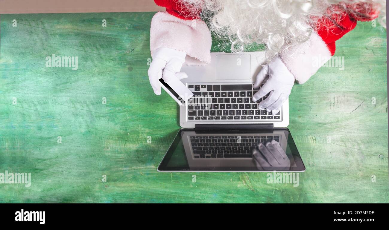 Vista dall'alto di Babbo Natale lavorando con le mani su un computer portatile che effettua acquisti con una carta di credito dorata, è possibile vedere un dettaglio della sua barba. Spazio di testo Foto Stock