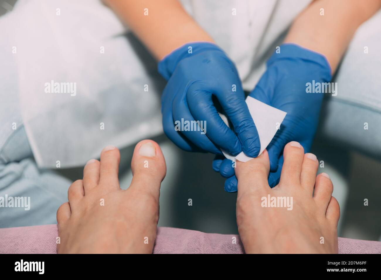 Pedicure processo in salone. Cura del piede e unghie. Sgrassare i chiodi con un panno e una soluzione. Master in guanti blu fa pedicure con manicure Foto Stock