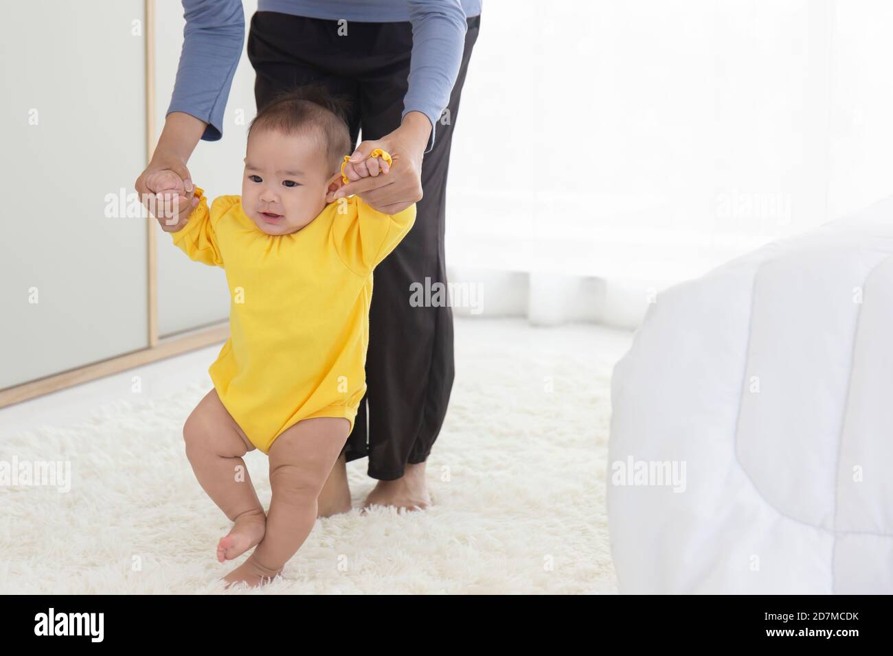 Una madre asiatica sta aiutando a sostenere il suo bambino ad imparare a camminare in modo gioioso. Foto Stock