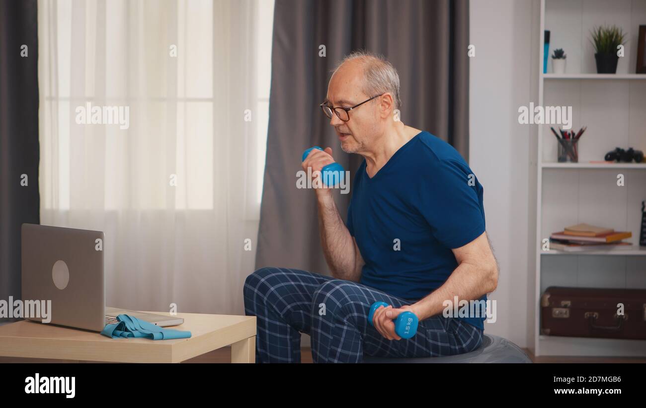 Allenamento sano dell'uomo anziano seguendo la lezione di fitness online. Anziano pensionato sano addestrando sport di salute a casa, esercitandosi attività di idoneità all'età anziana Foto Stock