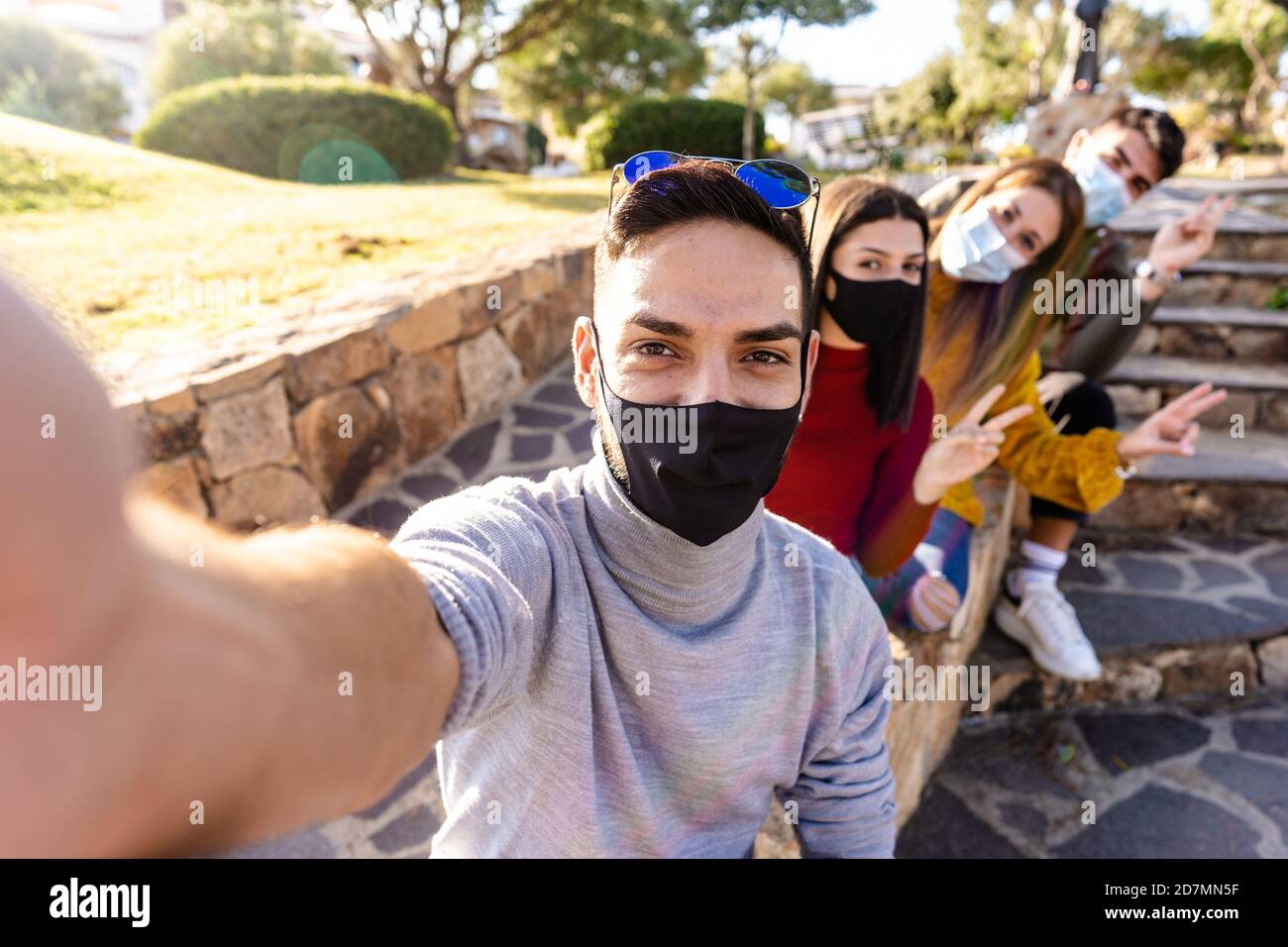 Ritratto di gruppo esterno di giovani felici con maschera medica - Millennial uomo prendere un selfie con i suoi amici schierati Dietro di lui - nuovo outdoo normale Foto Stock