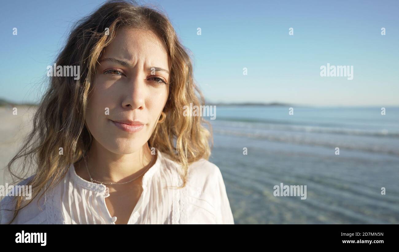 Faccia primo piano di giovane cute bionda caucasica che guarda la fotocamera al tramonto o all'alba in riva al mare con Una camicia bianca elegante - gente reale co Foto Stock