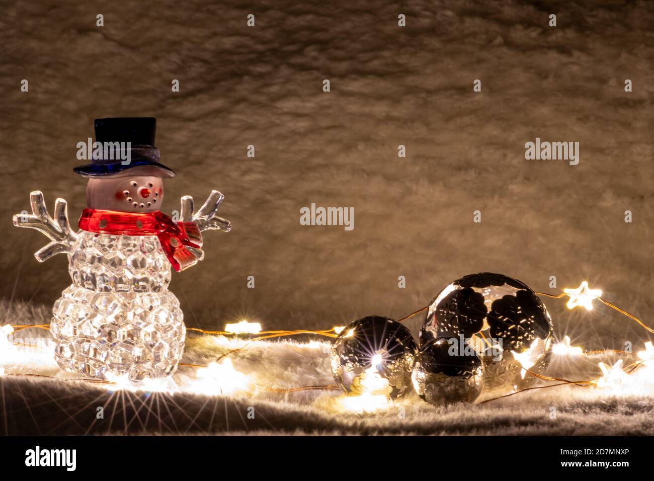 Pupazzo di neve di natale brillante con cappello nero e sciarpa rossa è illuminato su fondo di neve da luci fiabe luminose come illuminato decorazione di natale Foto Stock