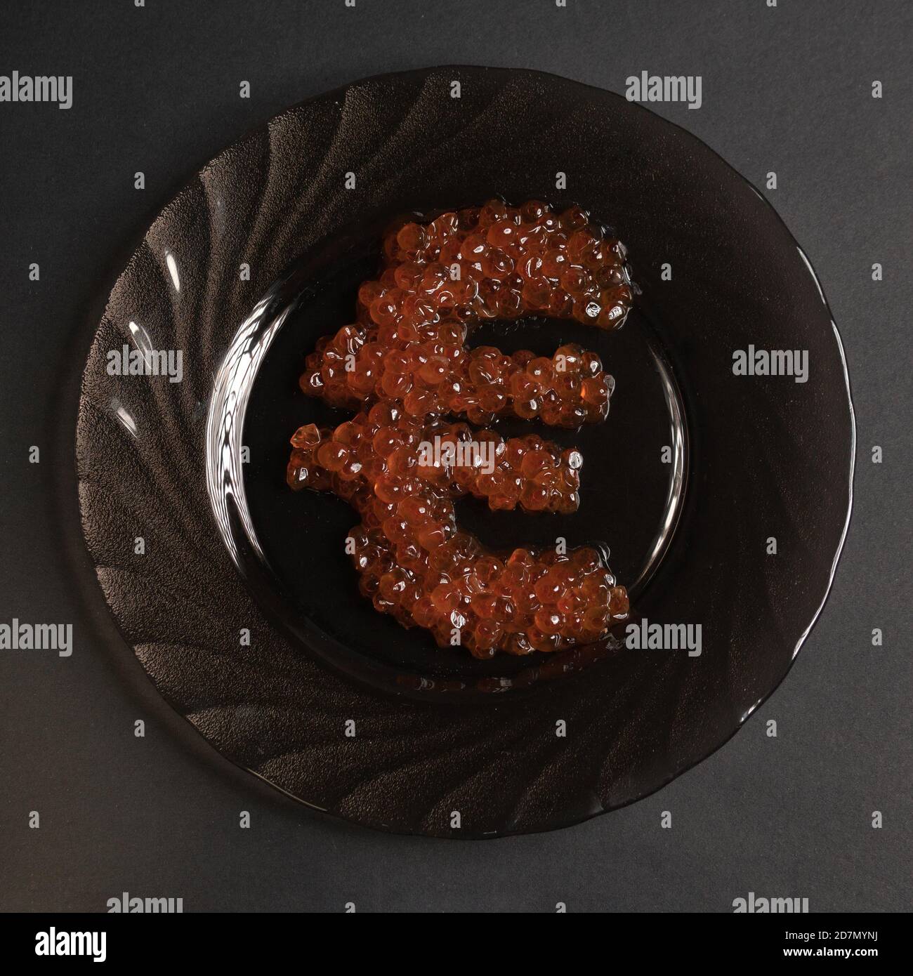 Il simbolo dell'euro è fatto di caviale rosso su una piastra nera su uno sfondo grigio che guarda dall'alto. Il cibo nei ristoranti d'élite del mondo è un simbolo Foto Stock